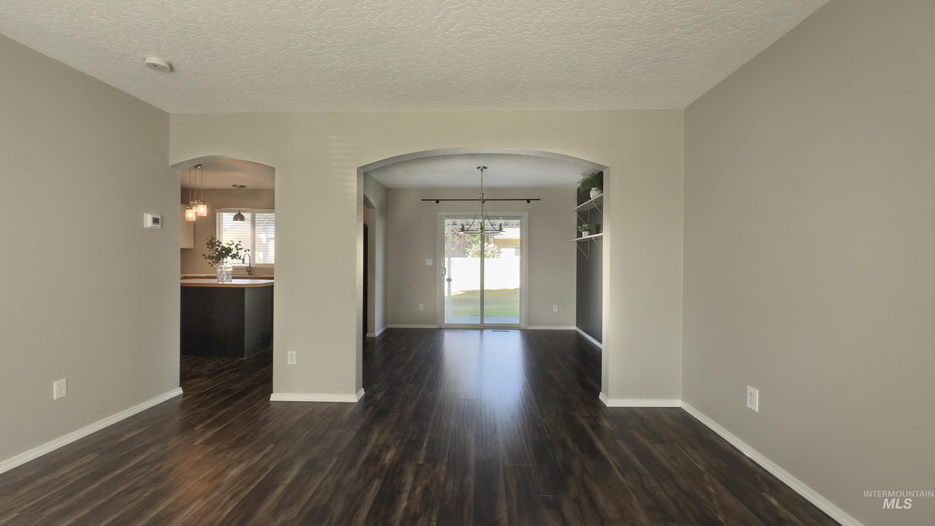 Unfurnished room featuring a chandelier, arched walkways, dark wood-style flooring, and a textured ceiling