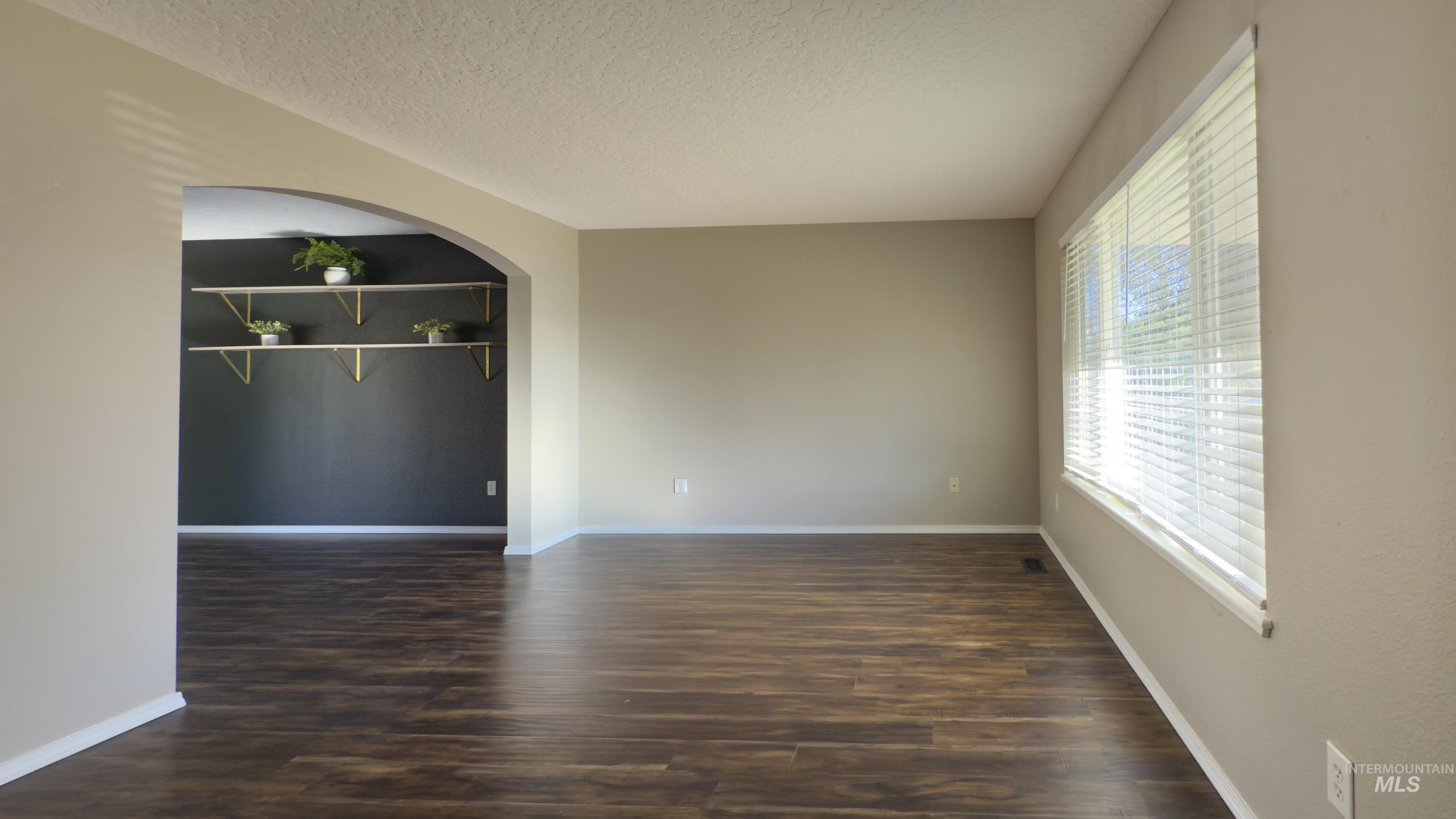 Unfurnished room with arched walkways, dark wood-type flooring, and a textured ceiling