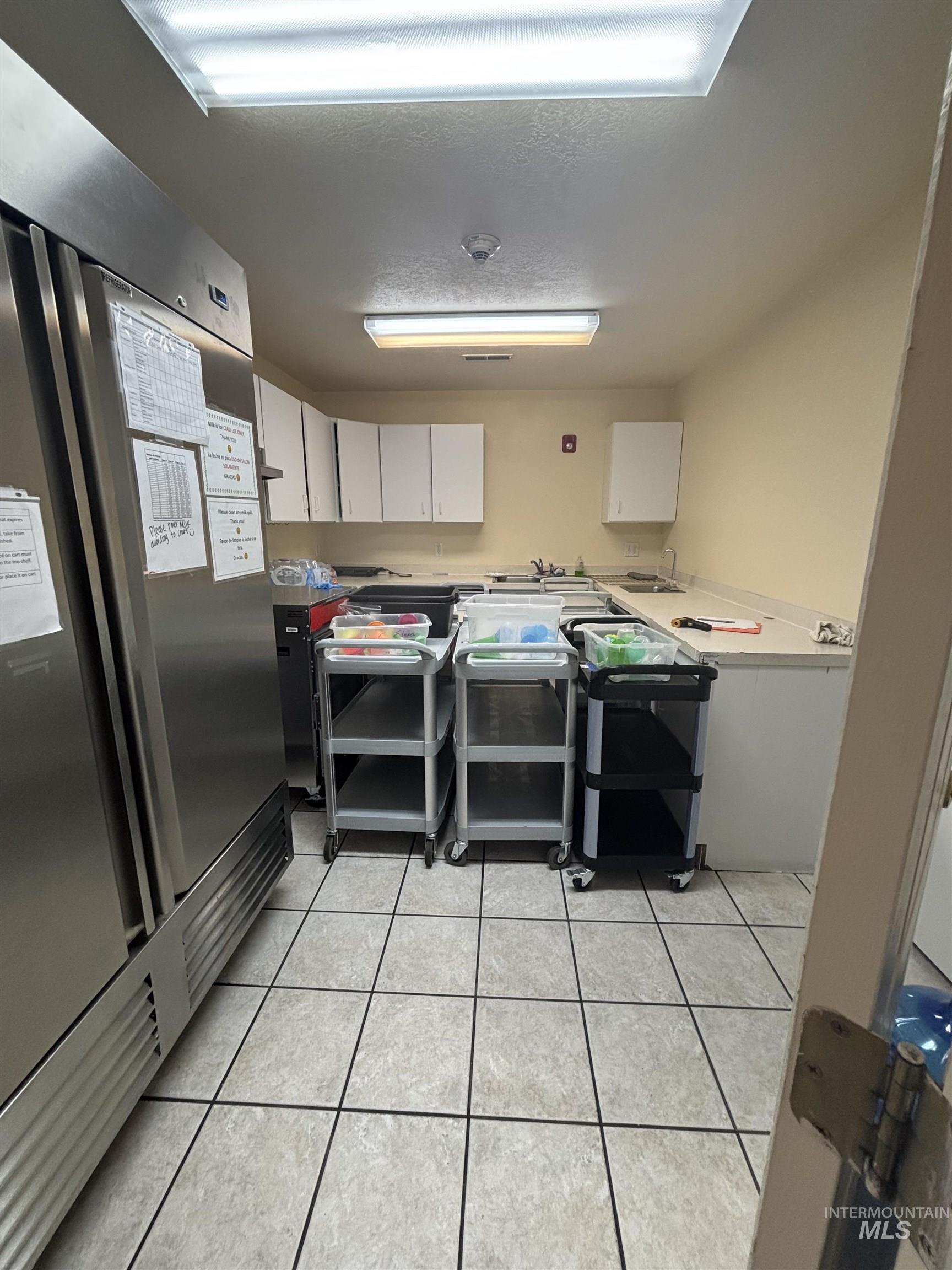 Kitchen featuring white cabinetry, stainless steel refrigerator, light tile patterned floors, light countertops, and a textured ceiling