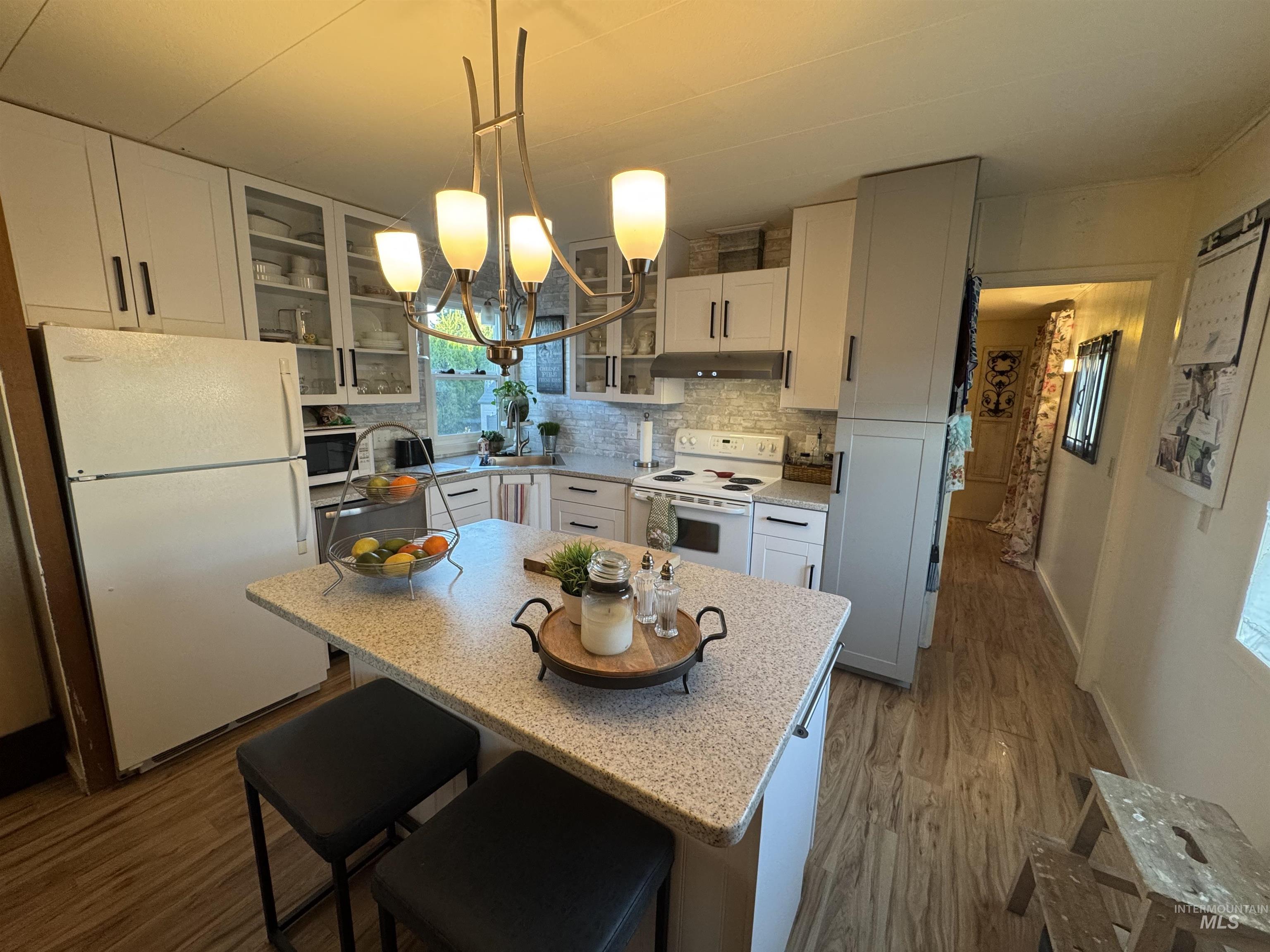 Kitchen with glass insert cabinets, dark wood-style floors, a breakfast bar area, white appliances, and pendant lighting