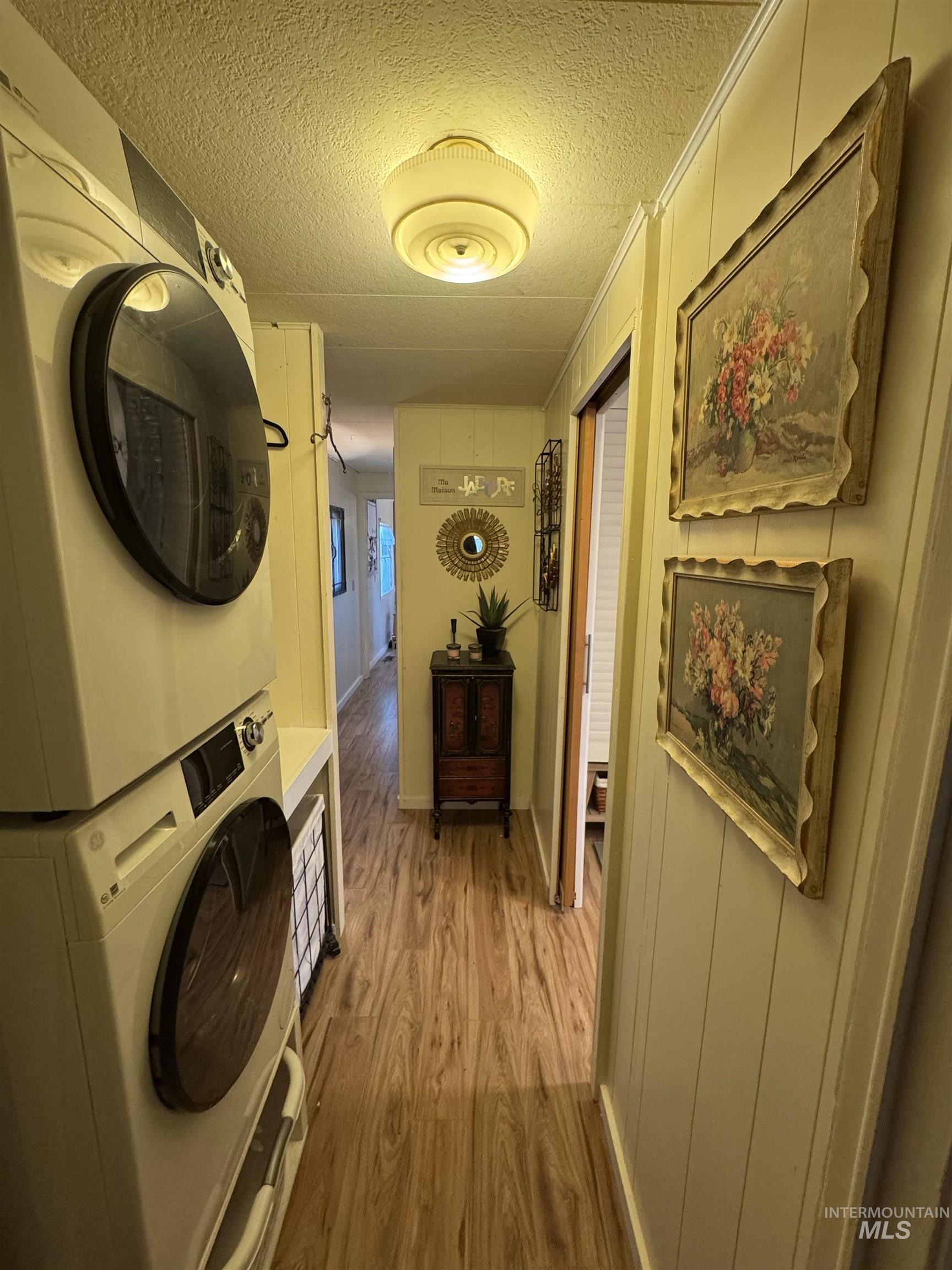Washroom with wood finished floors, a textured ceiling, and stacked washing machine and dryer