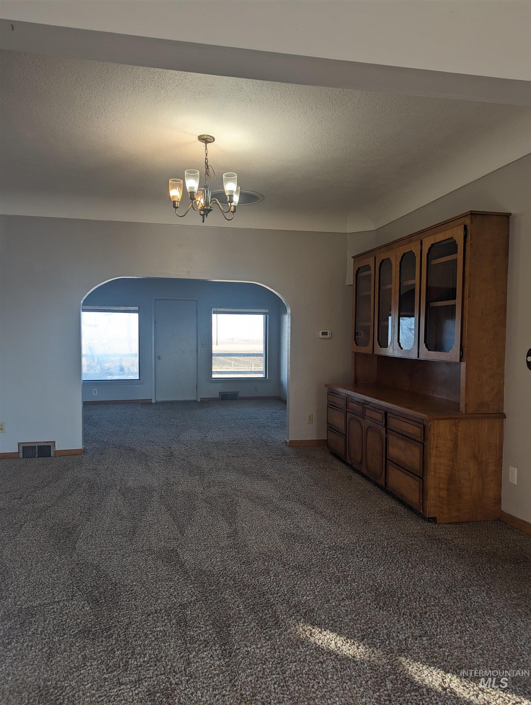 Unfurnished dining area with arched walkways, dark carpet, a chandelier, and a textured ceiling