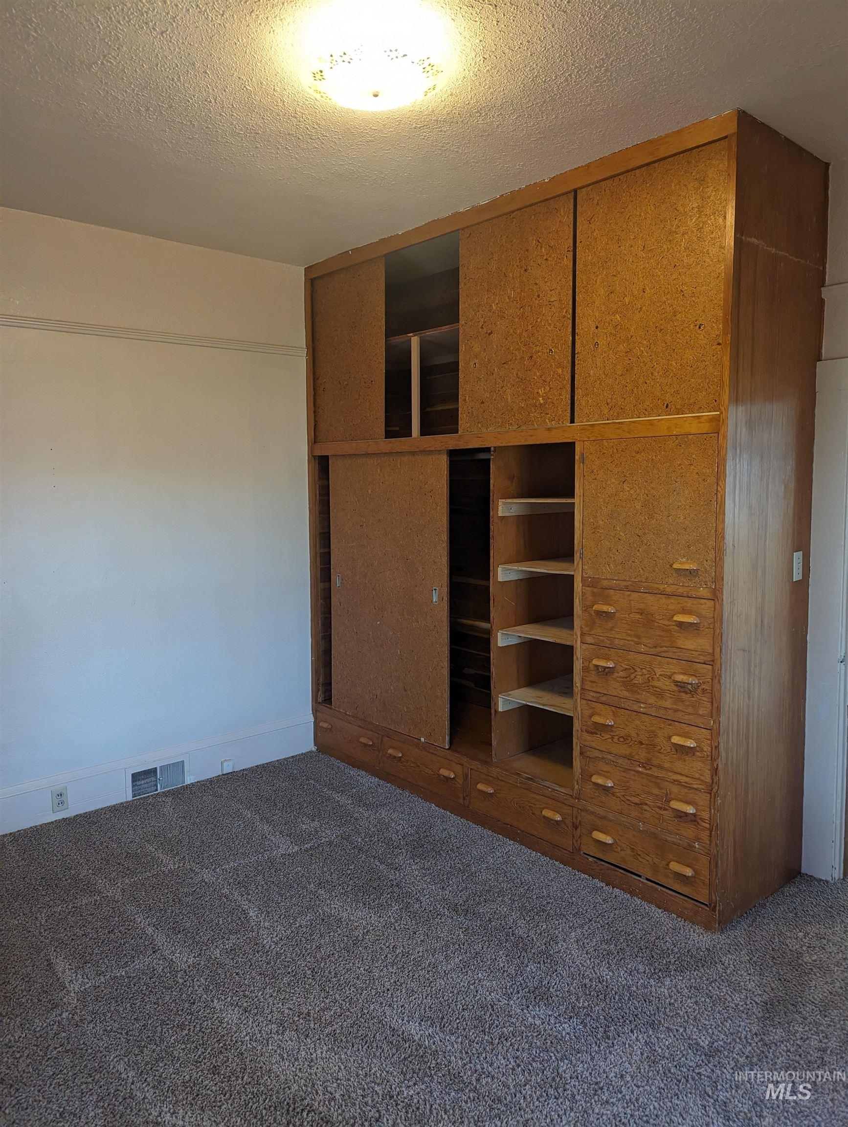 Unfurnished bedroom with a textured ceiling, dark colored carpet, and a closet