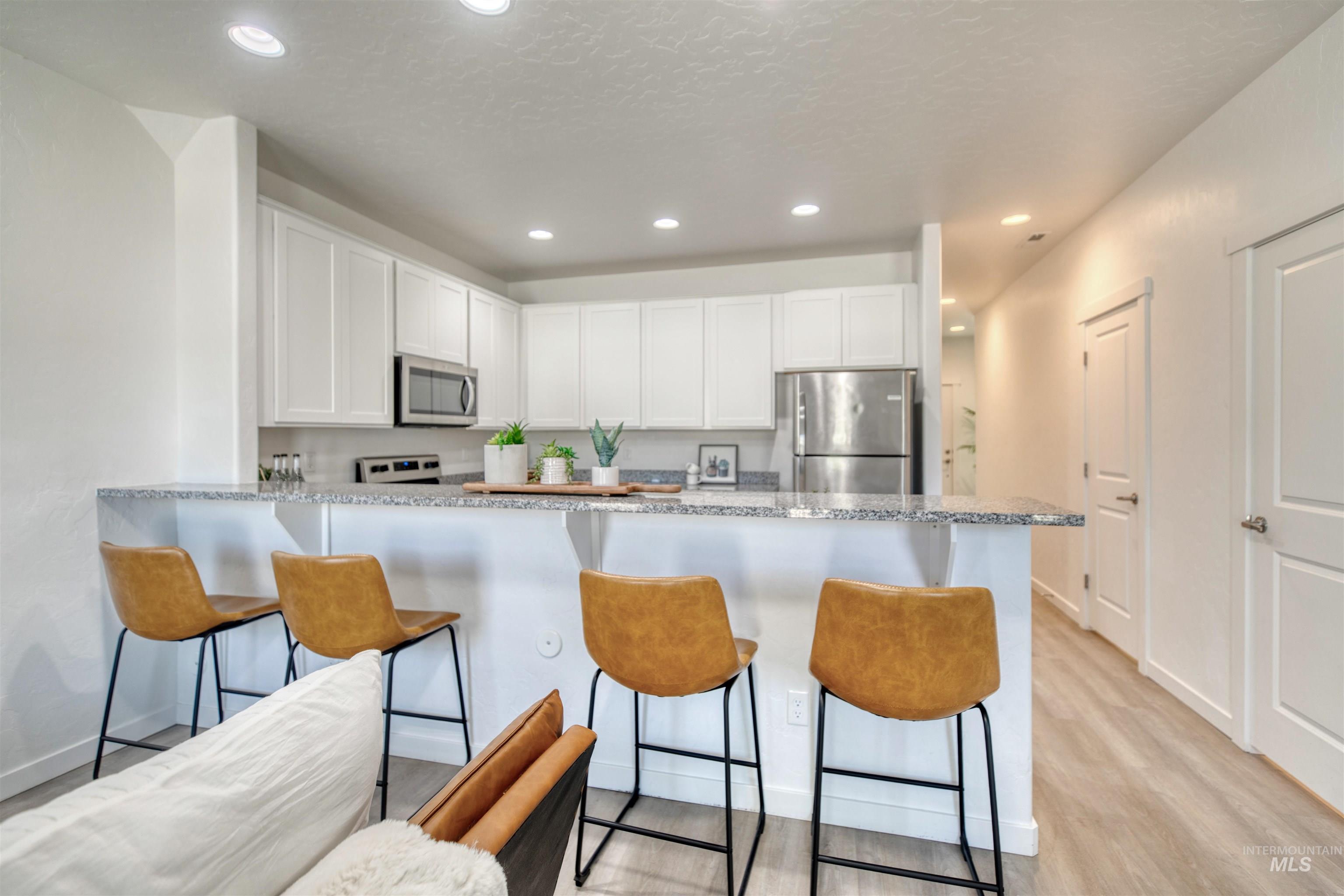 Kitchen with a breakfast bar area, white cabinets, recessed lighting, a peninsula, and appliances with stainless steel finishes