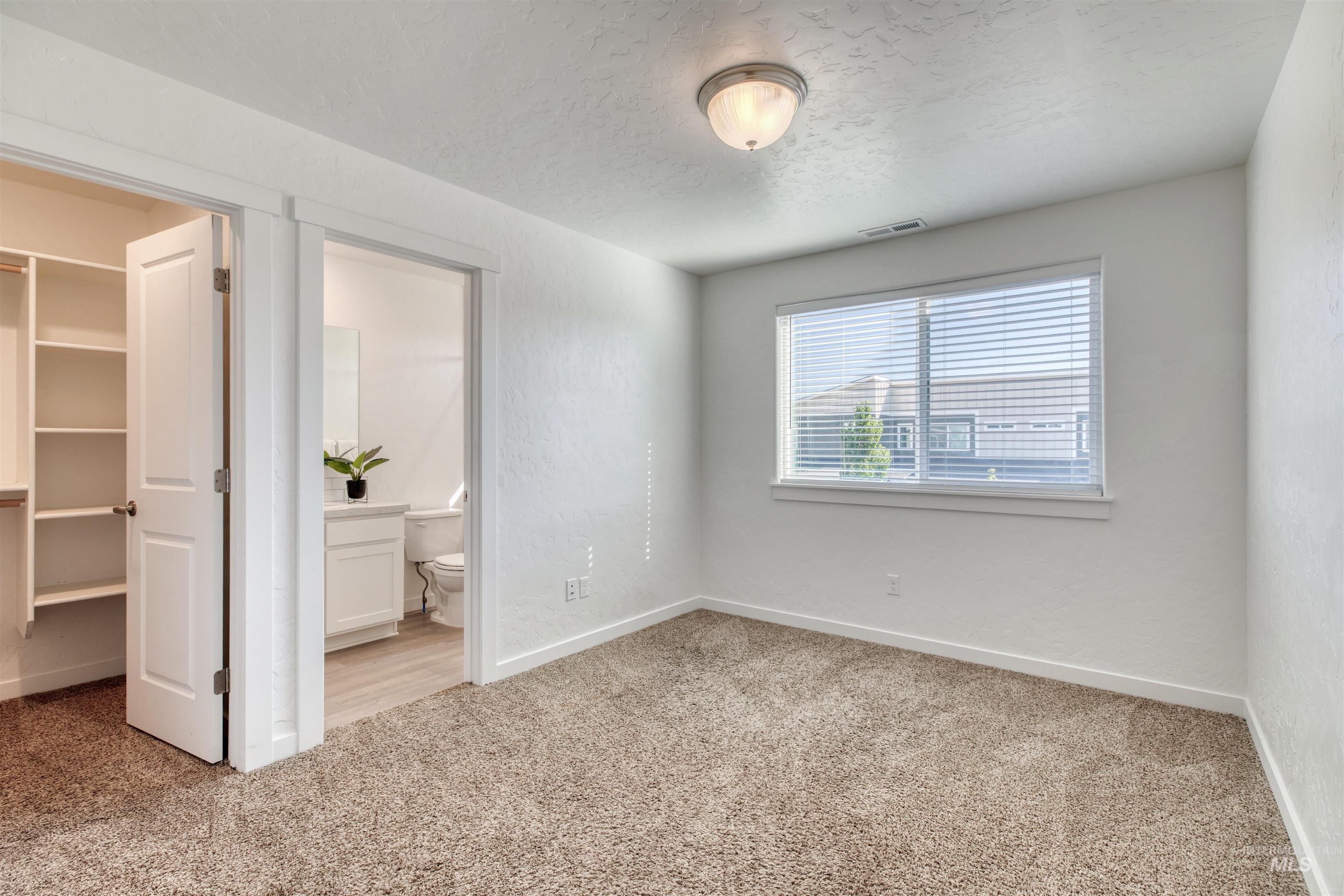 Unfurnished bedroom with light carpet, a walk in closet, and a textured ceiling