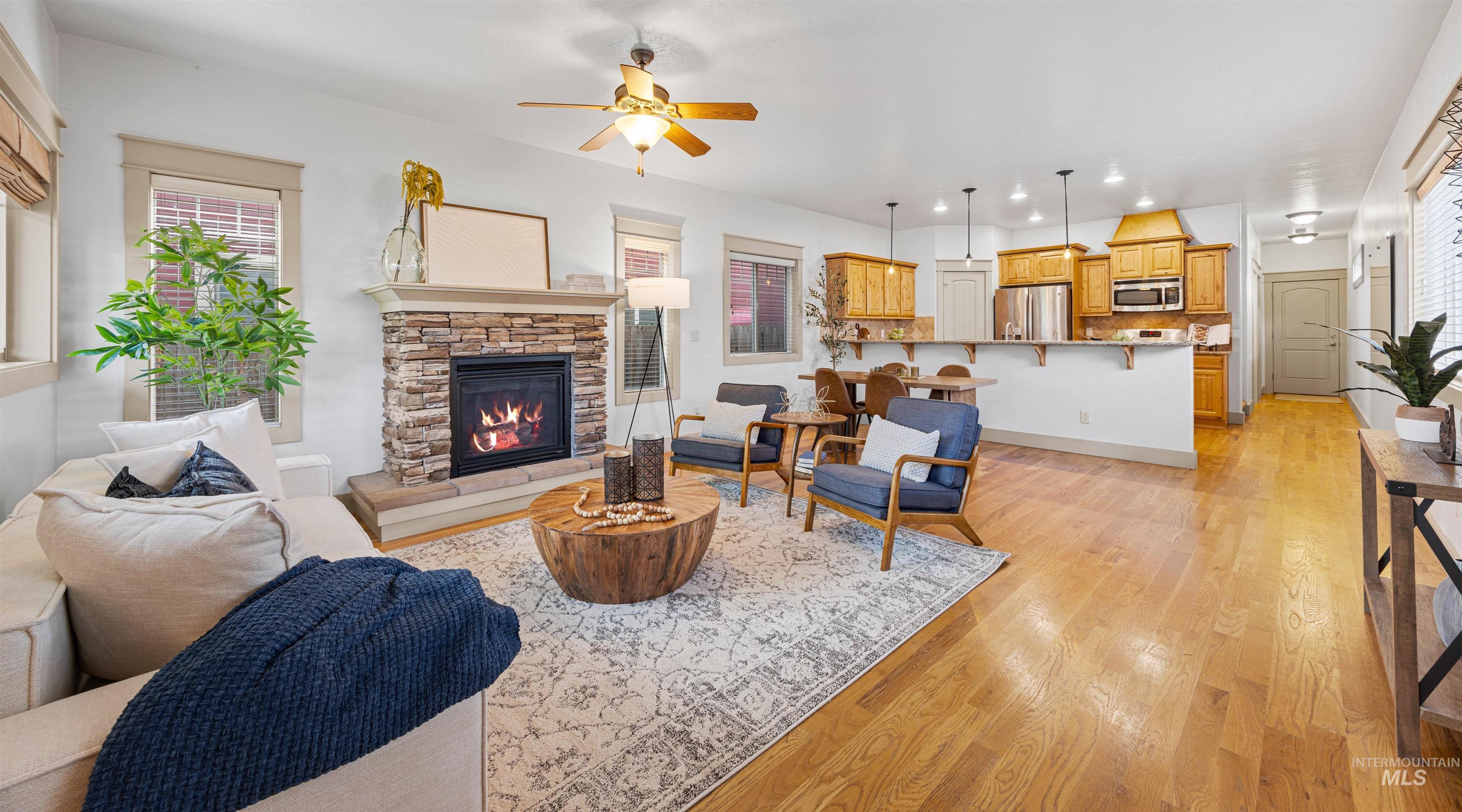 Living area with light wood-style floors, a stone fireplace, a ceiling fan, and recessed lighting