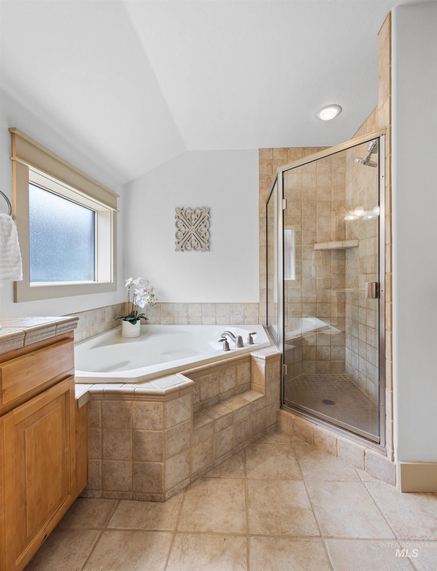 Bathroom with a bath, a stall shower, lofted ceiling, vanity, and light tile patterned floors