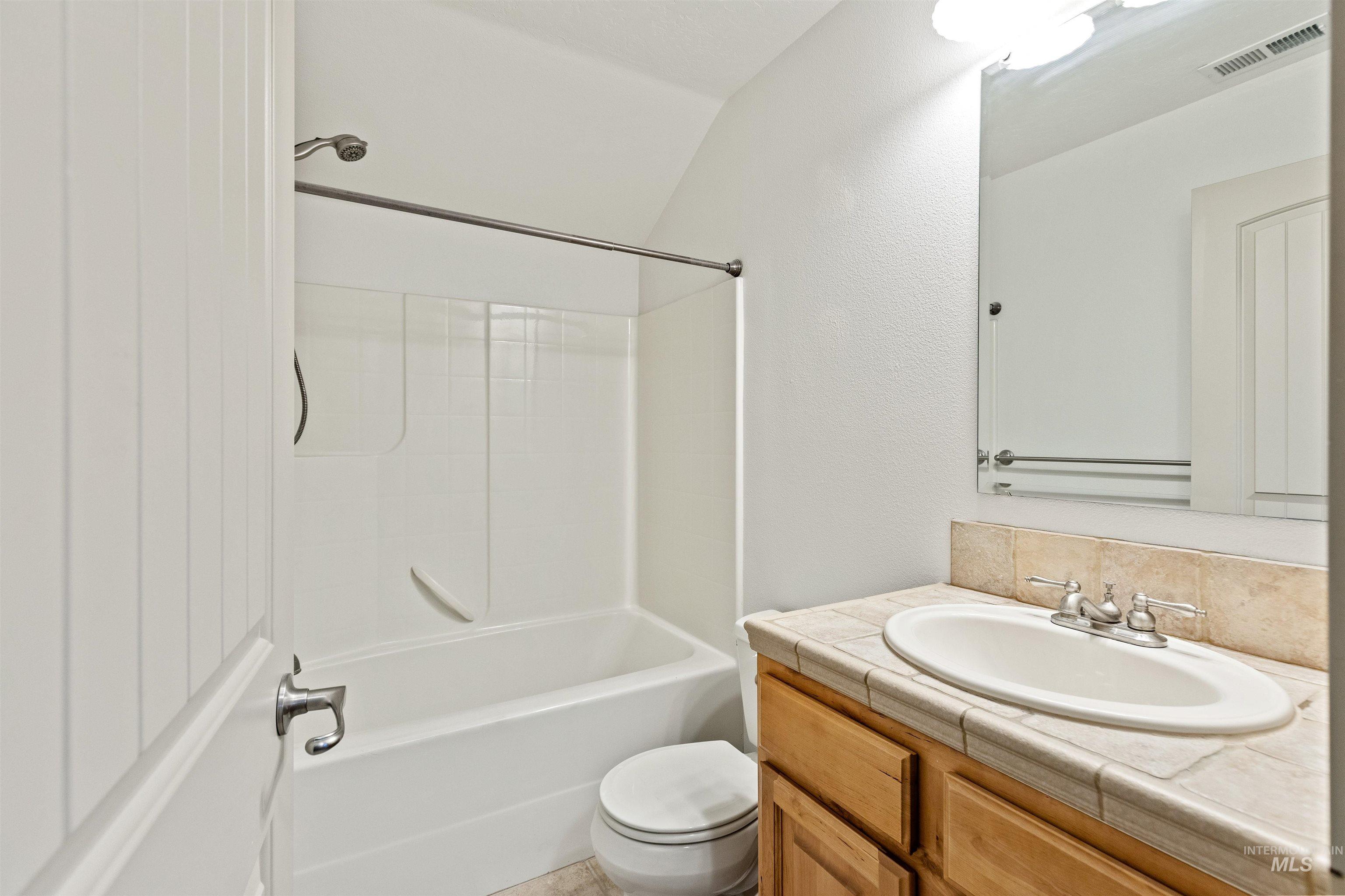 Bathroom with vanity, shower / bathtub combination, tasteful backsplash, and lofted ceiling