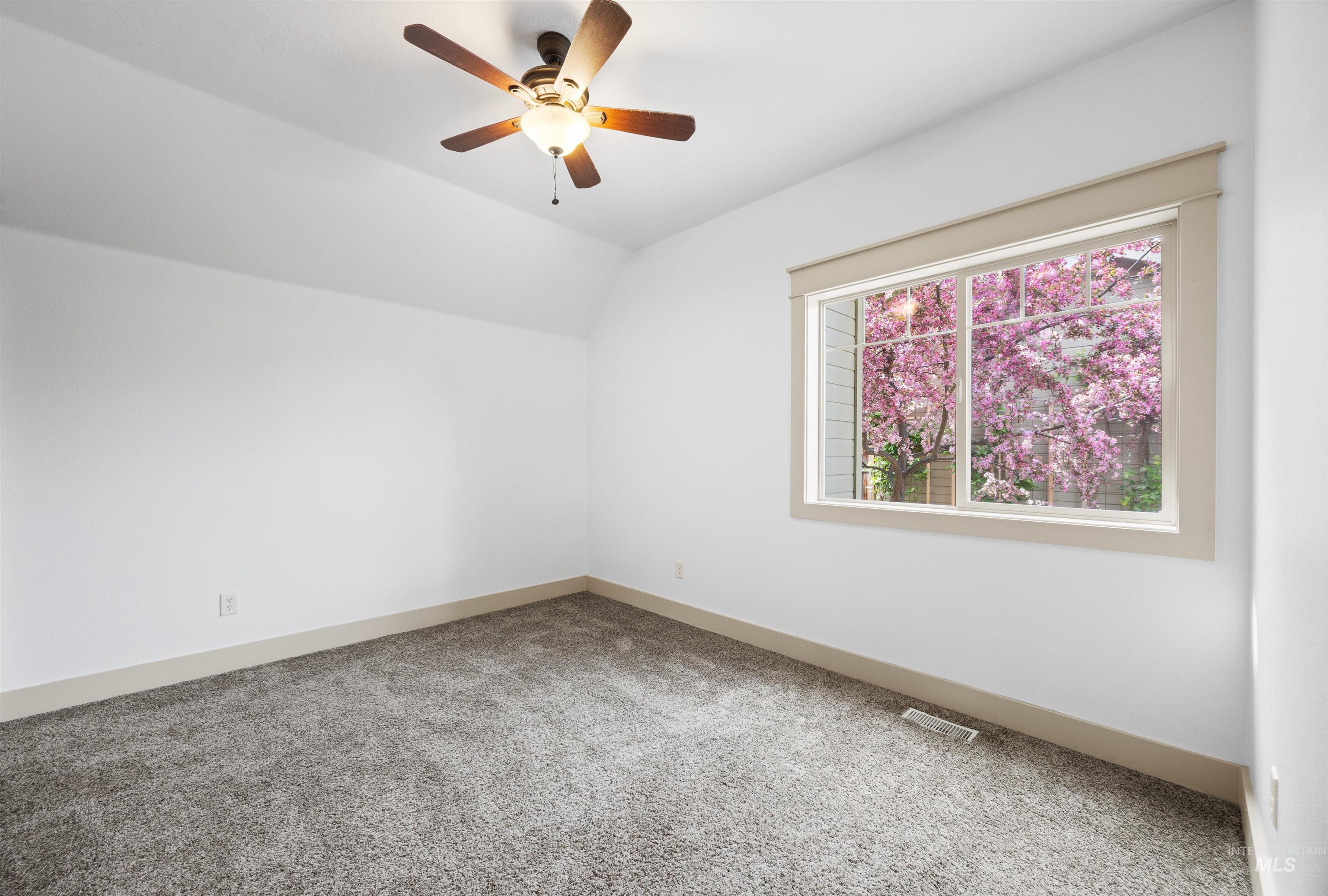 Carpeted spare room featuring vaulted ceiling and a ceiling fan