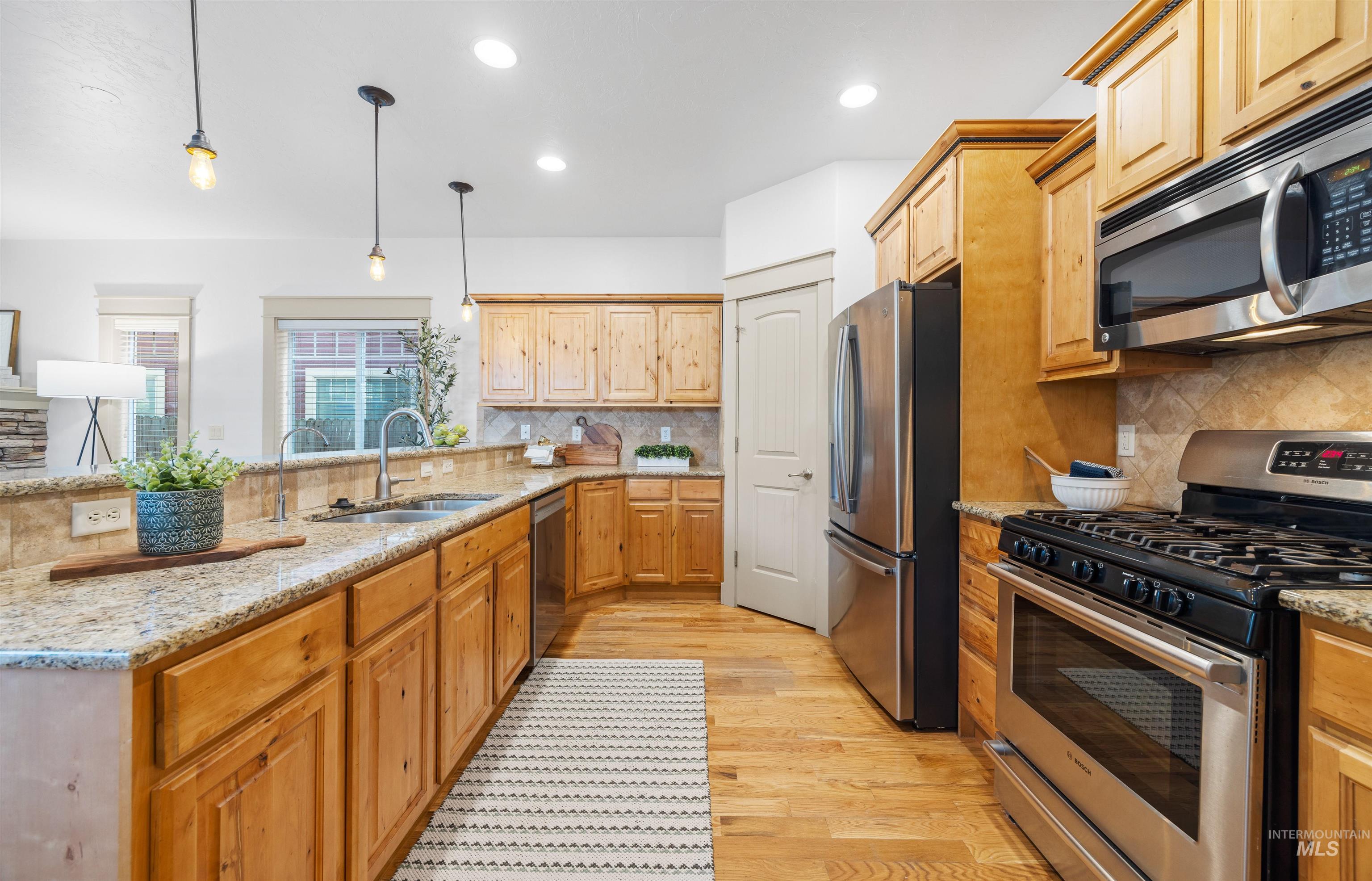 Kitchen featuring appliances with stainless steel finishes, light wood-style floors, hanging light fixtures, light stone counters, and backsplash