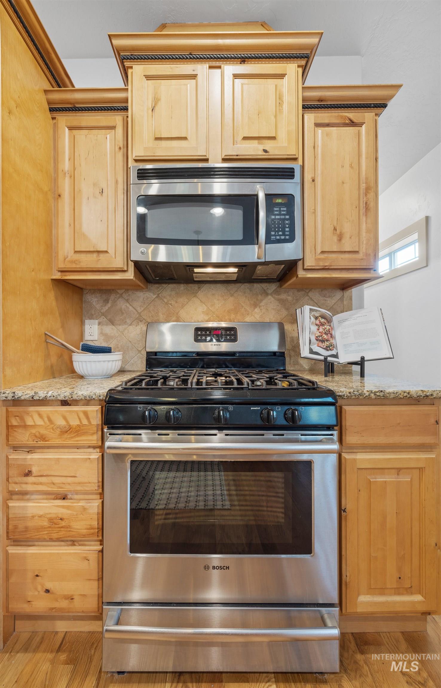 Kitchen with appliances with stainless steel finishes, light brown cabinetry, backsplash, and light stone countertops