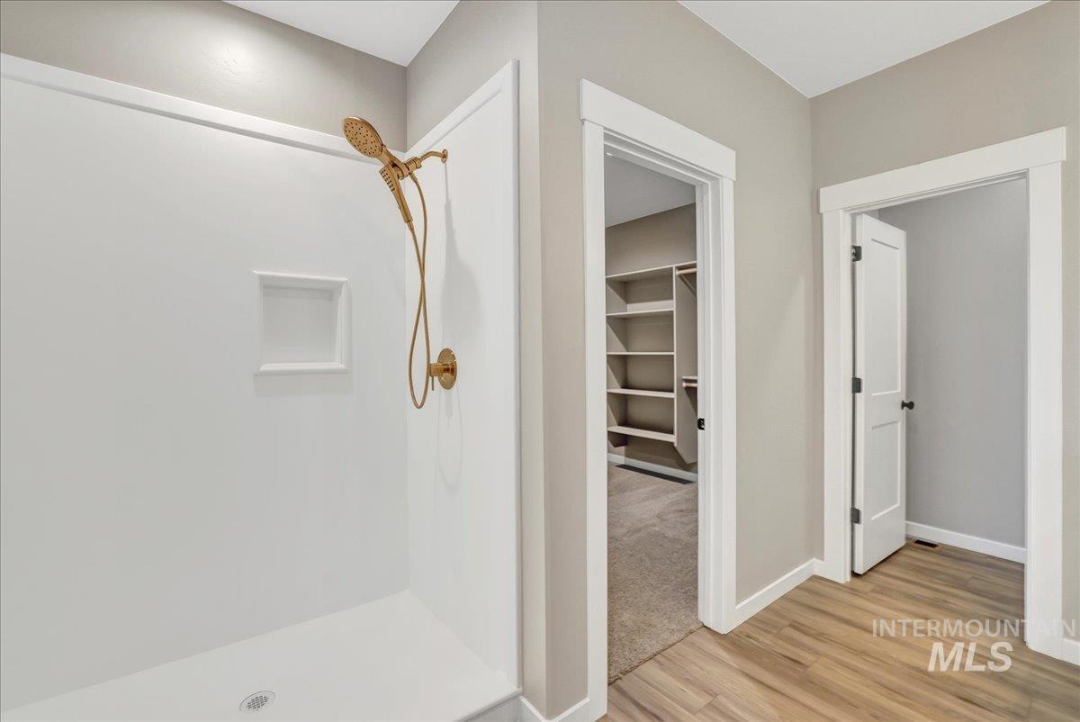 Full bathroom featuring a shower stall, light wood-type flooring, and a spacious closet