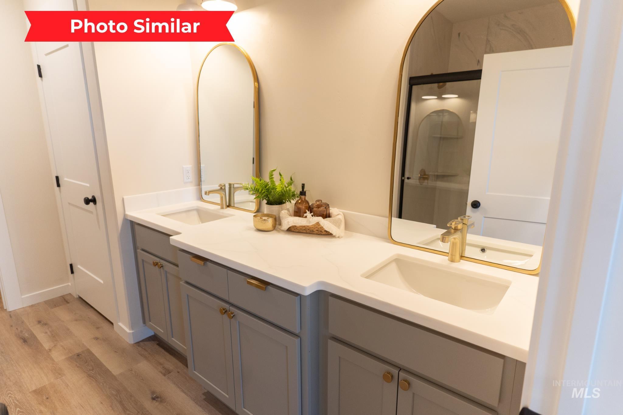 Full bathroom with double vanity, light wood-style floors, and an enclosed shower