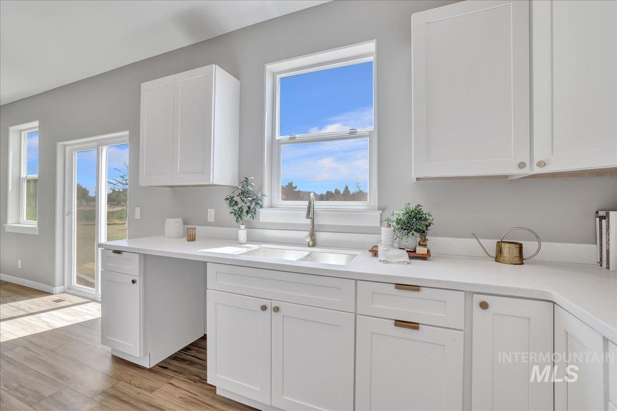 Kitchen featuring white cabinets, healthy amount of natural light, light wood finished floors, and light stone countertops