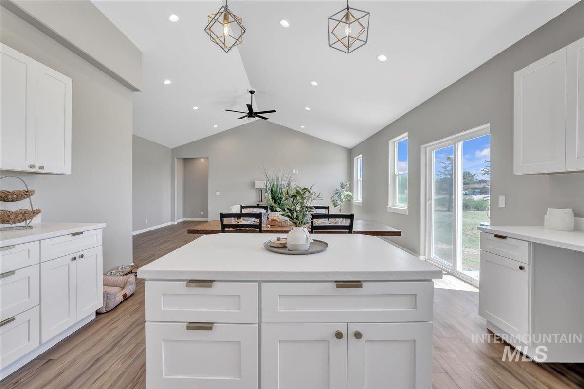 Kitchen featuring white cabinets, open floor plan, light wood-style floors, a kitchen island, and lofted ceiling
