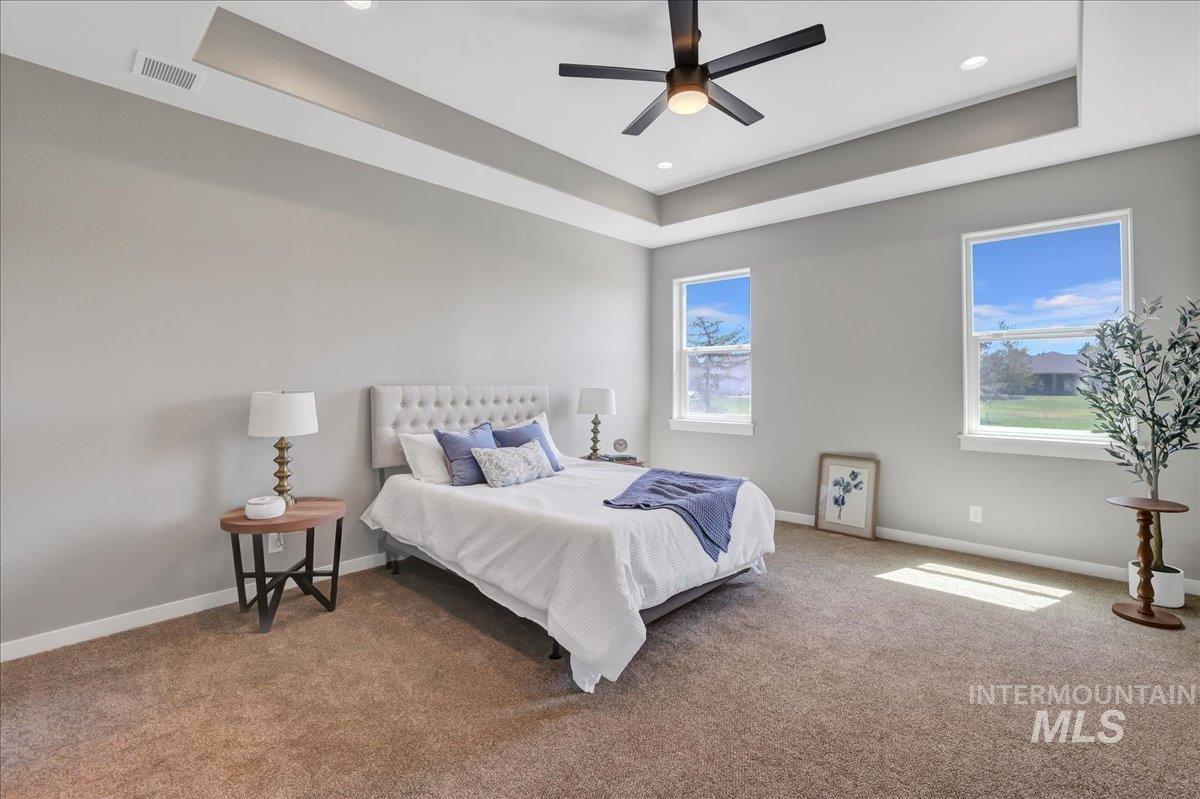 Bedroom with a raised ceiling, carpet flooring, and ceiling fan
