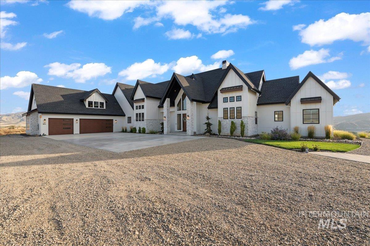 Modern farmhouse with stone siding, concrete driveway, board and batten siding, a chimney, and a shingled roof