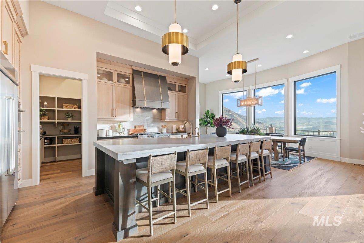 Kitchen with a kitchen breakfast bar, hanging light fixtures, tasteful backsplash, light wood-type flooring, and glass insert cabinets