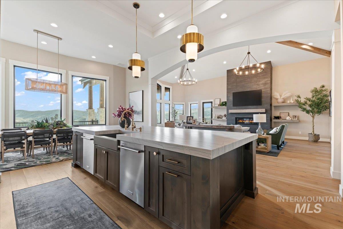 Kitchen featuring dark brown cabinetry, a kitchen island with sink, light wood-style floors, hanging light fixtures, and light countertops