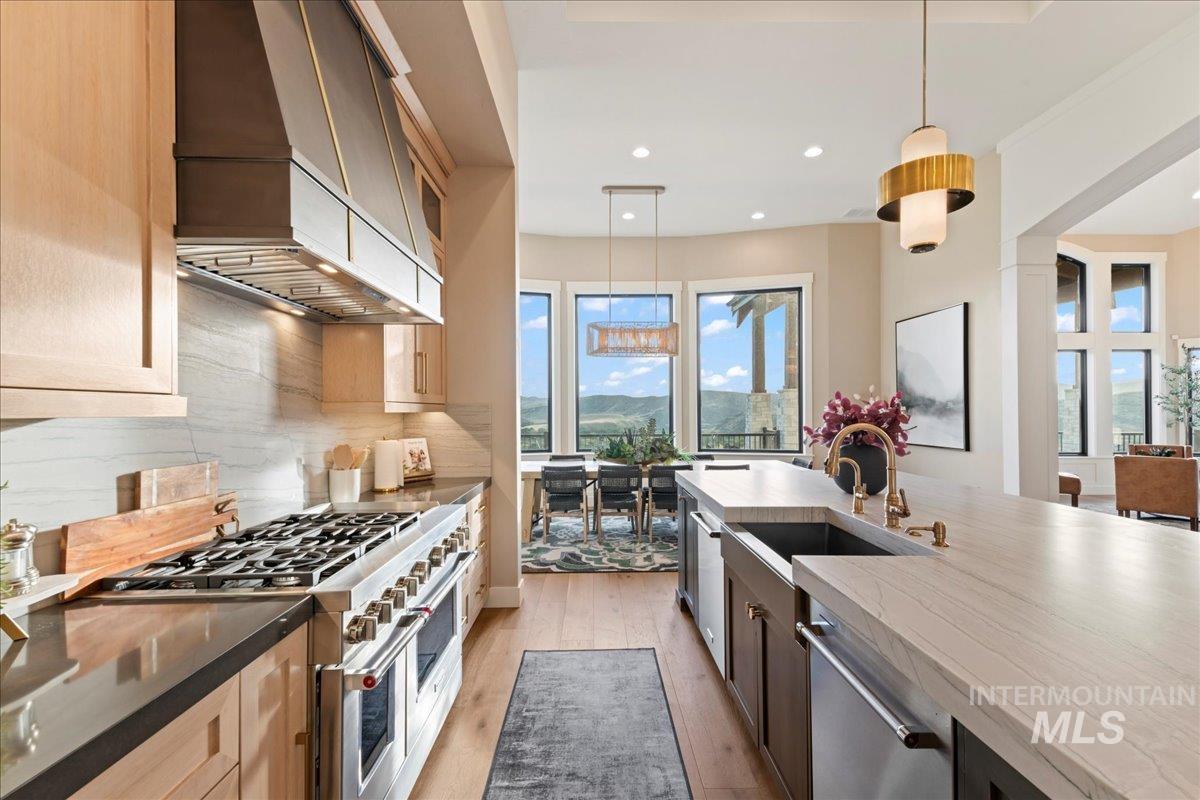 Kitchen featuring pendant lighting, stainless steel appliances, custom range hood, light wood-style floors, and healthy amount of natural light