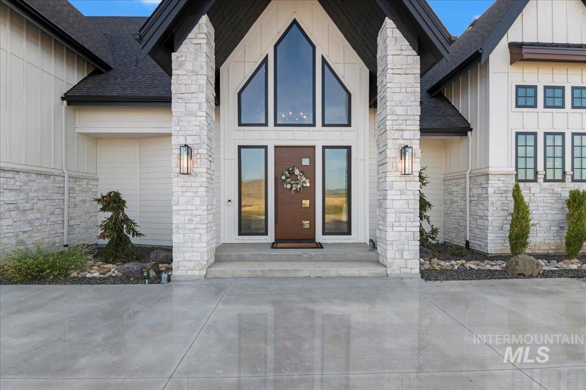 Doorway to property with stone siding, board and batten siding, and roof with shingles