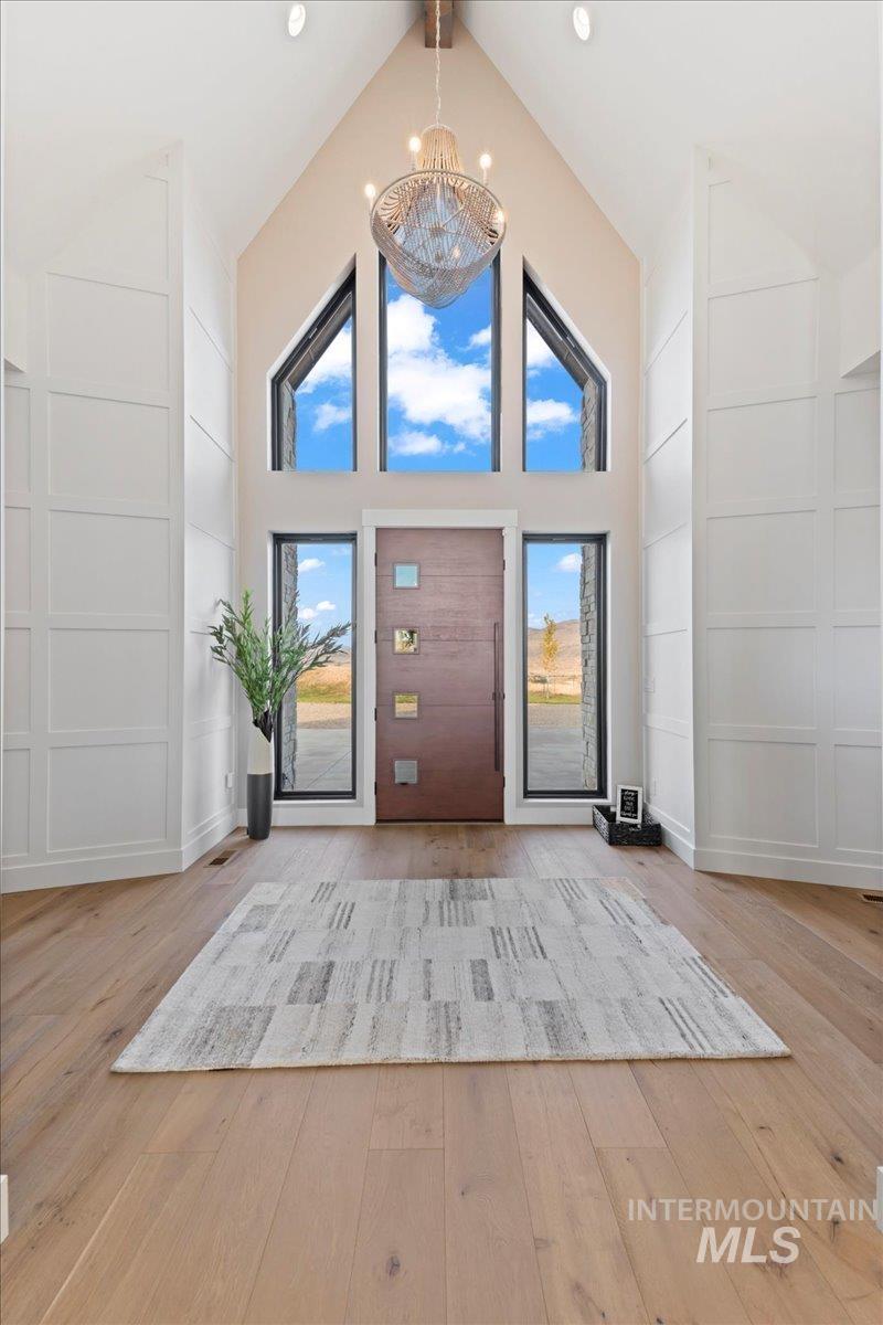 Entrance foyer featuring light wood-style flooring, a decorative wall, a chandelier, and high vaulted ceiling