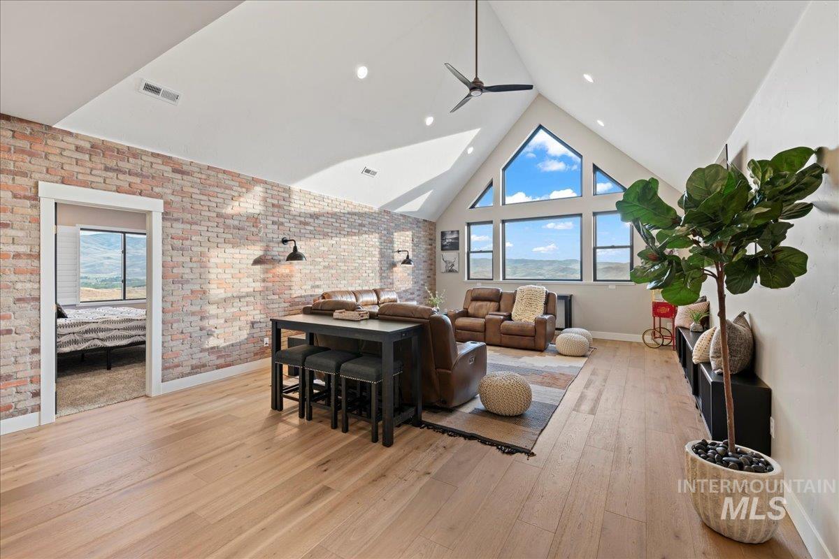 Living room featuring high vaulted ceiling, brick wall, light wood-style floors, and a ceiling fan