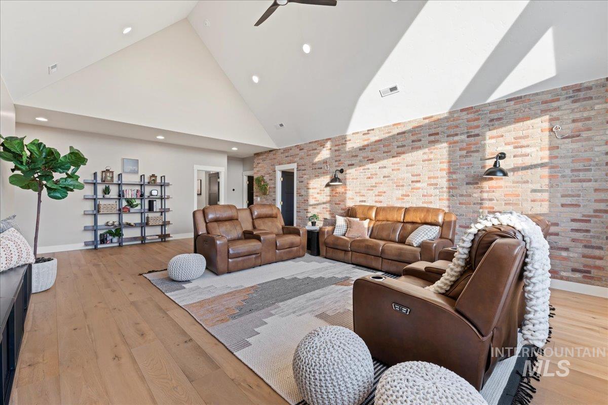 Living area featuring brick wall, high vaulted ceiling, a ceiling fan, light wood-style flooring, and recessed lighting