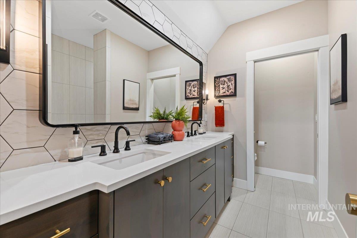 Bathroom featuring double vanity, light tile patterned floors, tasteful backsplash, and lofted ceiling