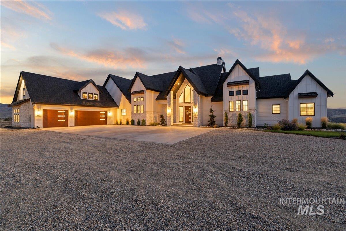 Modern inspired farmhouse featuring board and batten siding, driveway, stone siding, a chimney, and a garage