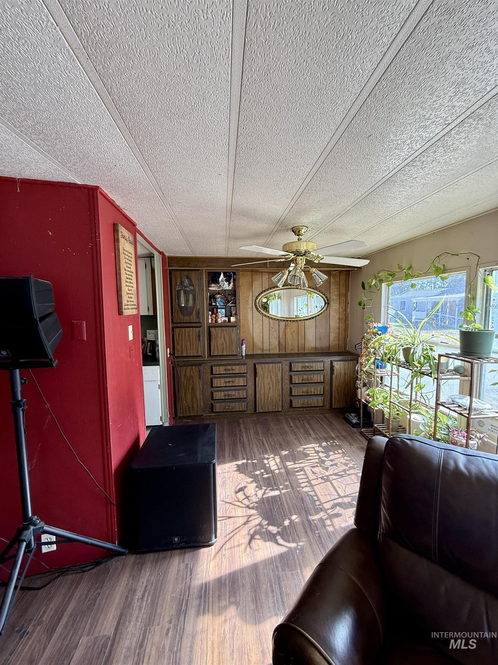 Living room with wood finished floors, ceiling fan, wood walls, and a textured ceiling