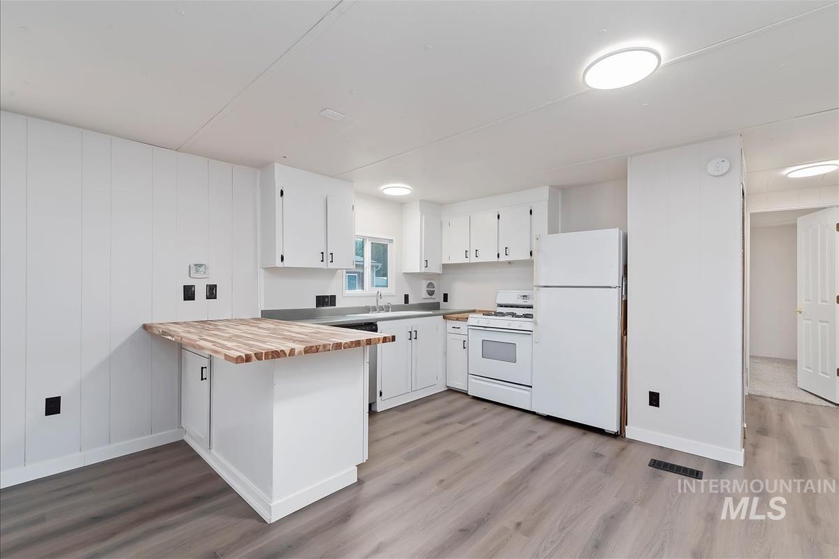 Kitchen with butcher block countertops, a peninsula, white appliances, white cabinets, and light wood-style flooring