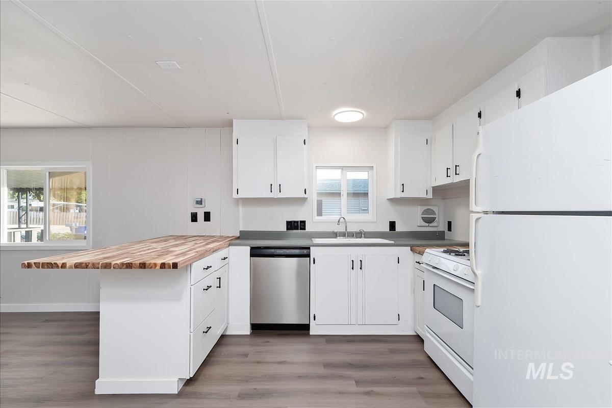 Kitchen with white appliances, a peninsula, butcher block counters, light wood-style flooring, and white cabinets