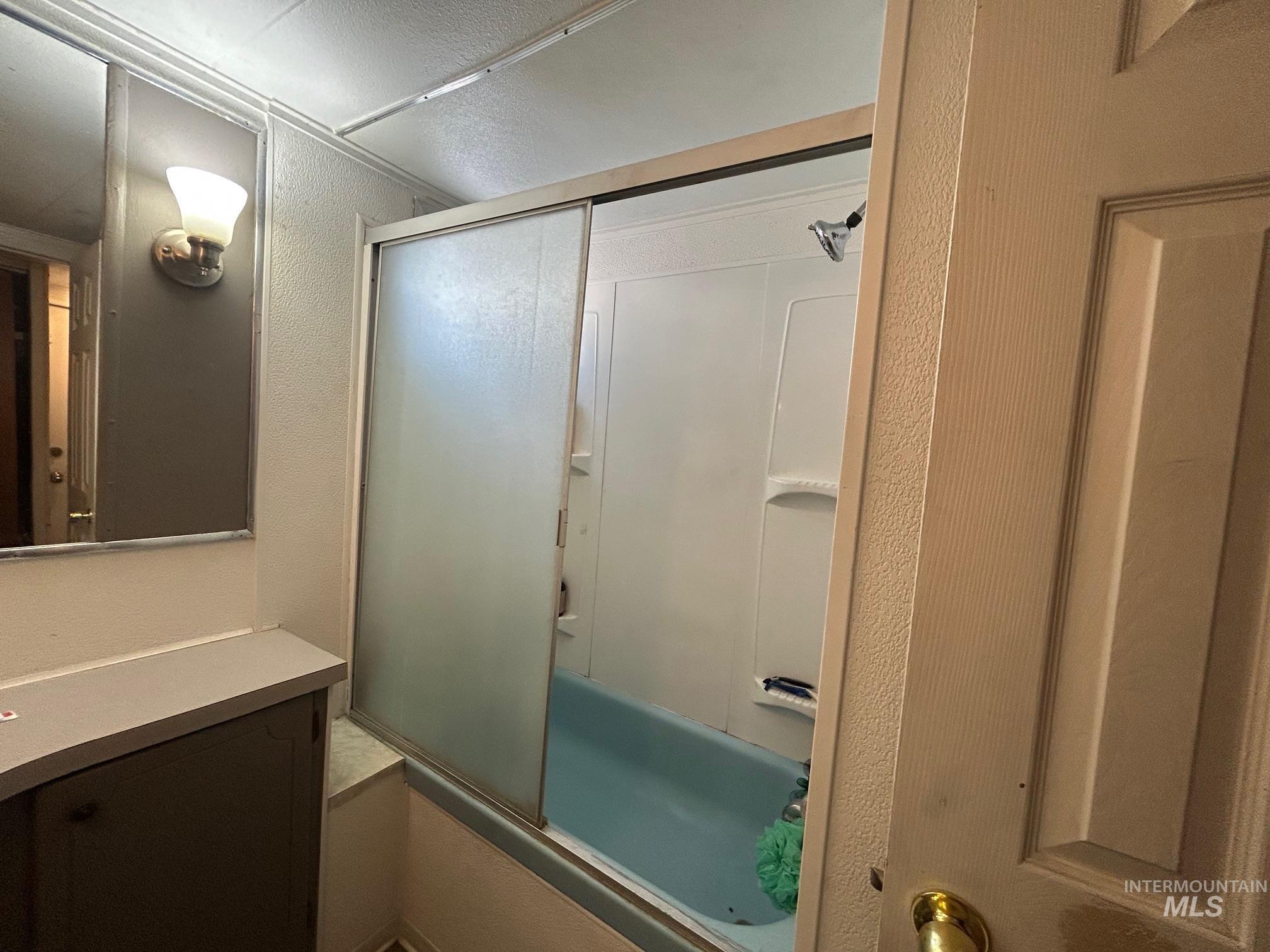 Bathroom with combined bath / shower with glass door and a textured wall