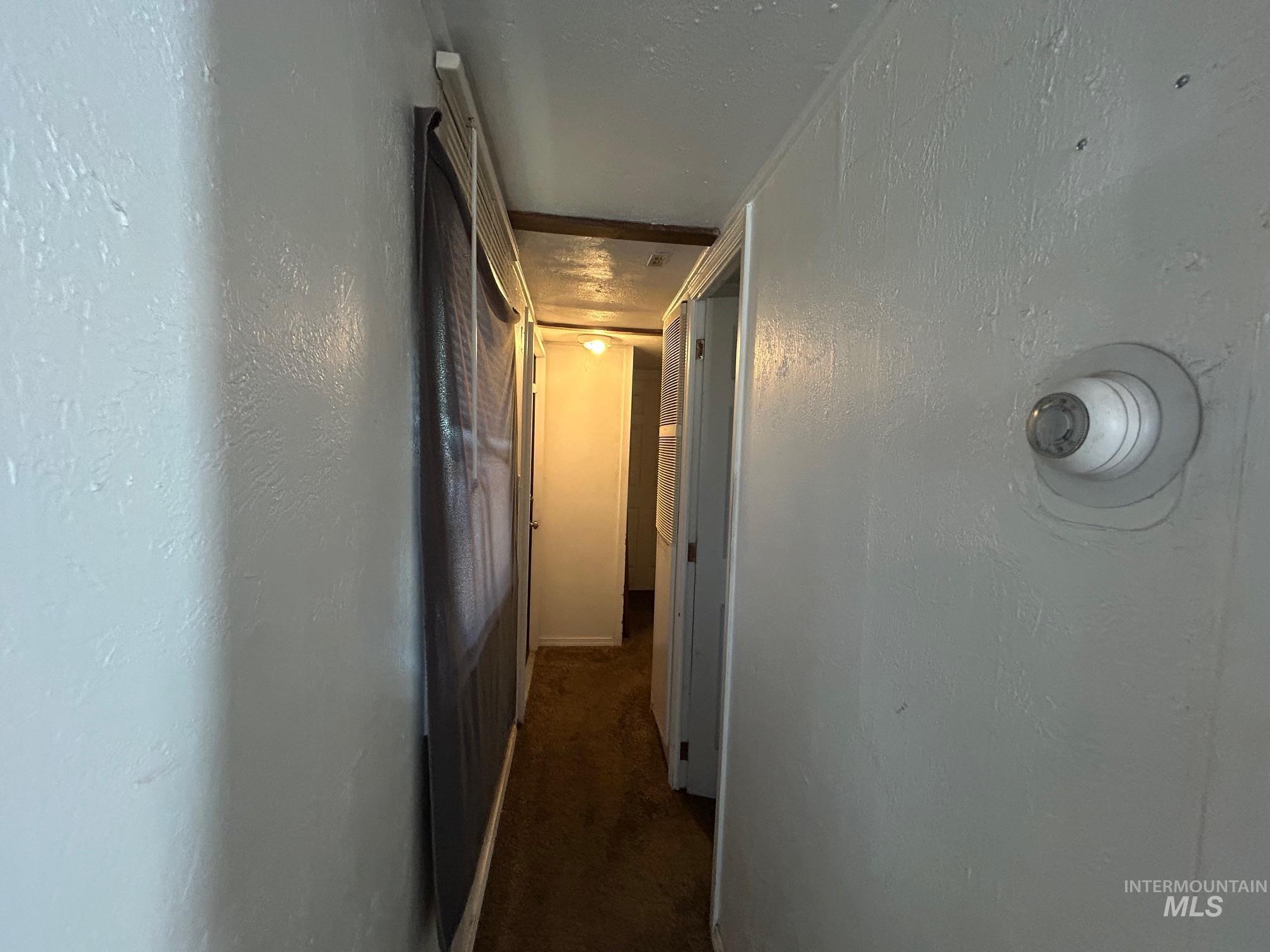 Hallway featuring dark colored carpet and a textured wall