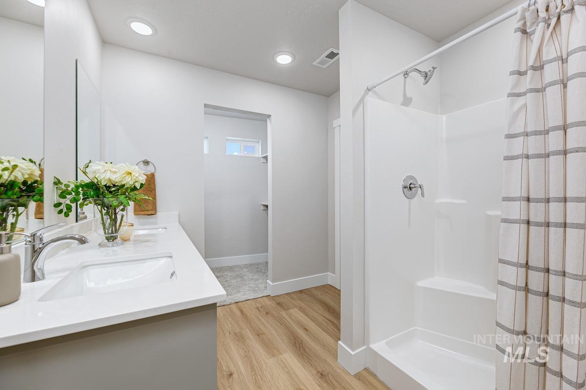 Bathroom featuring double vanity, a shower stall, light wood-style floors, and recessed lighting