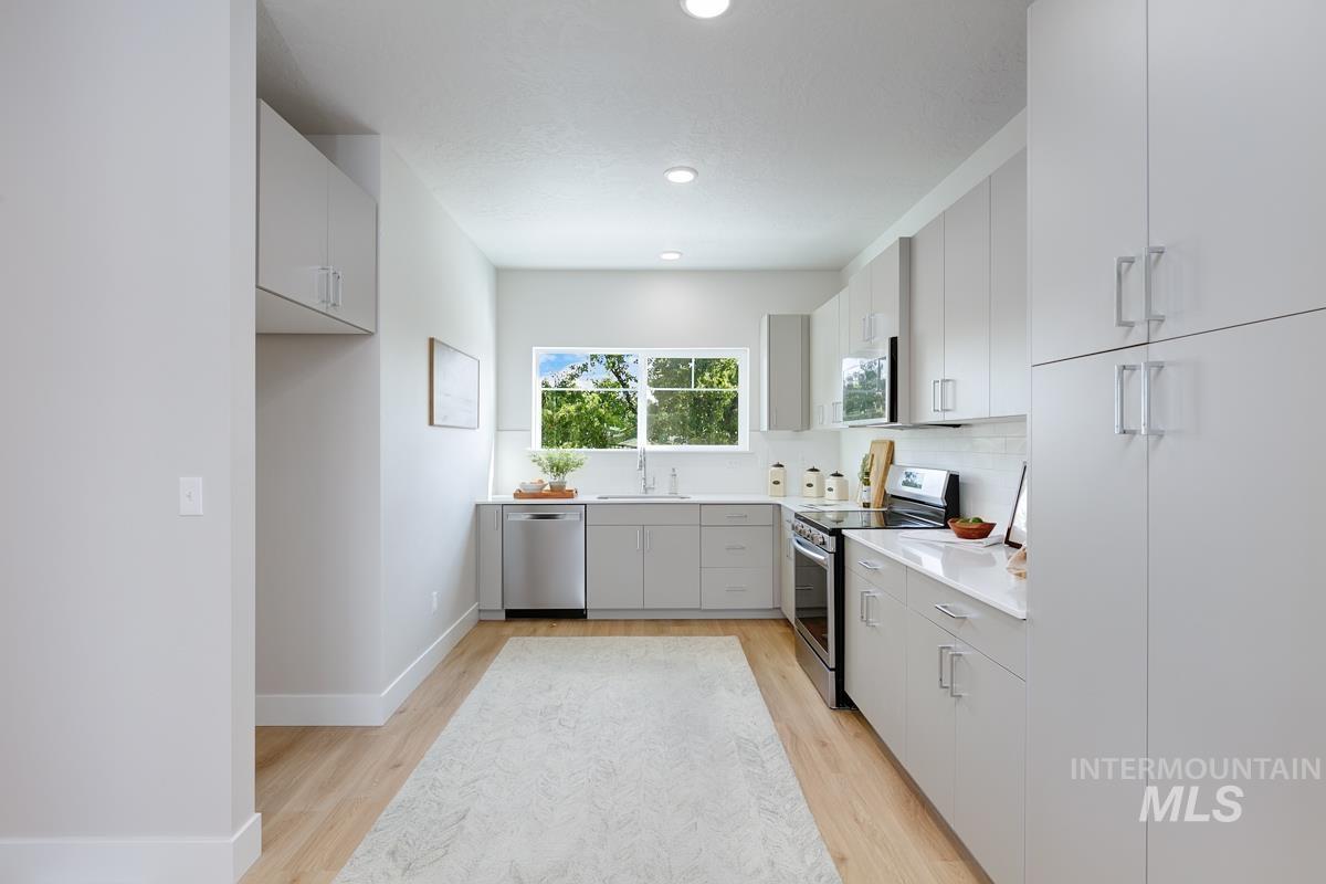 Kitchen with gray cabinets, appliances with stainless steel finishes, light wood finished floors, backsplash, and recessed lighting