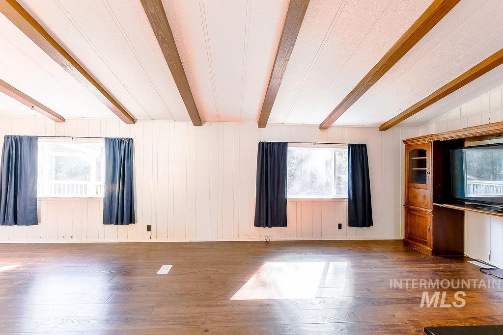 Unfurnished living room with wooden walls, hardwood / wood-style floors, and beam ceiling
