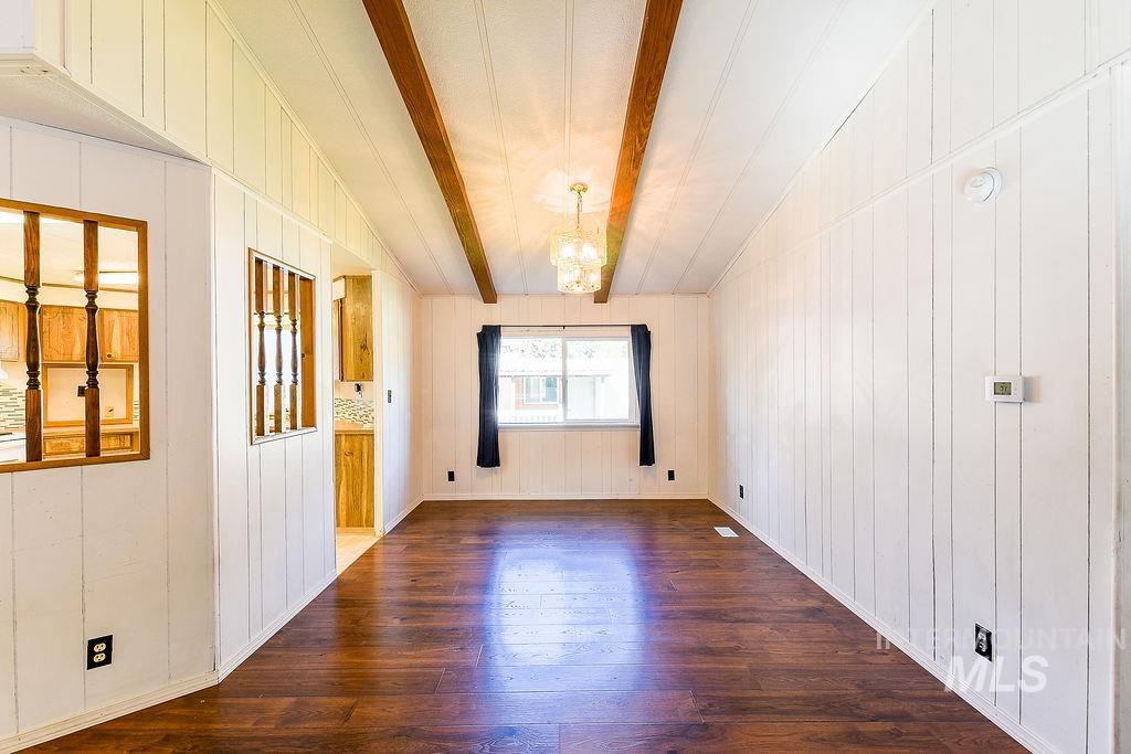 Unfurnished room featuring beam ceiling, a chandelier, dark wood finished floors, and wood walls