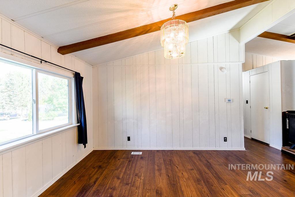 Empty room featuring wooden walls, dark wood-style flooring, and a chandelier