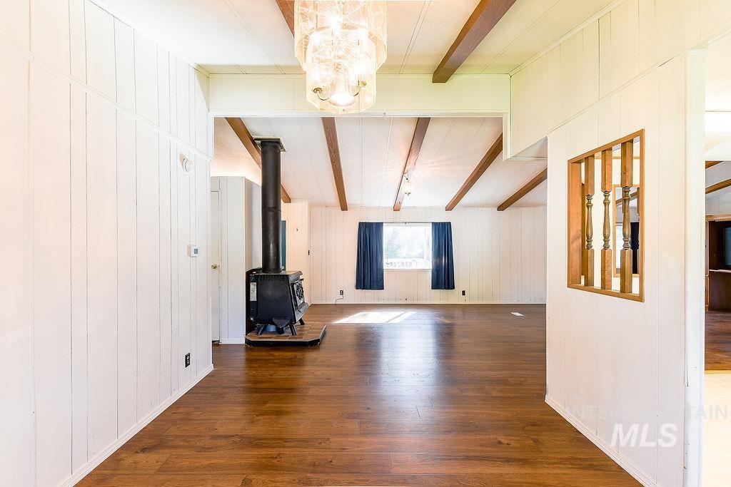 Unfurnished living room with wooden walls, dark wood finished floors, beamed ceiling, a wood stove, and a chandelier