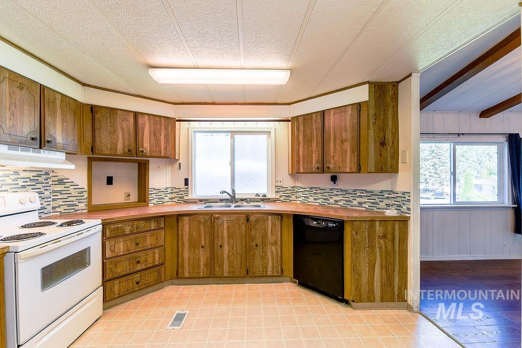 Kitchen with white electric range, dishwasher, under cabinet range hood, tasteful backsplash, and wood walls