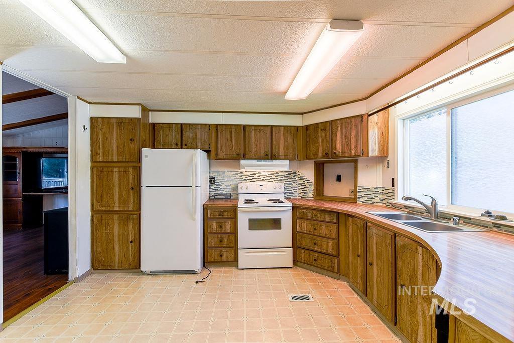 Kitchen featuring white appliances, decorative backsplash, brown cabinetry, light countertops, and under cabinet range hood