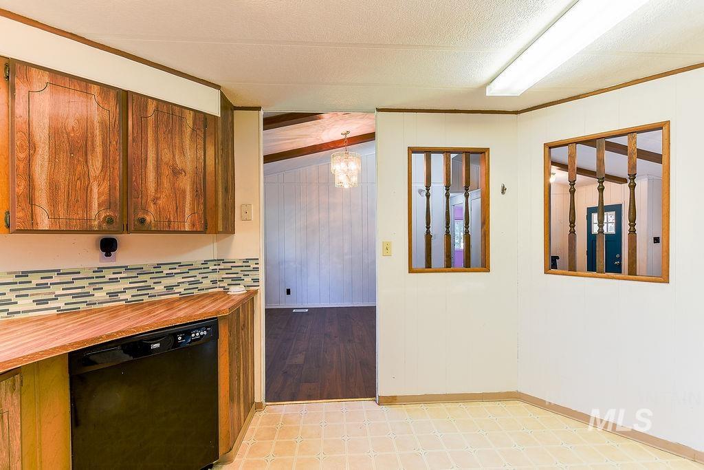Kitchen with dishwasher, wooden walls, brown cabinets, a chandelier, and crown molding