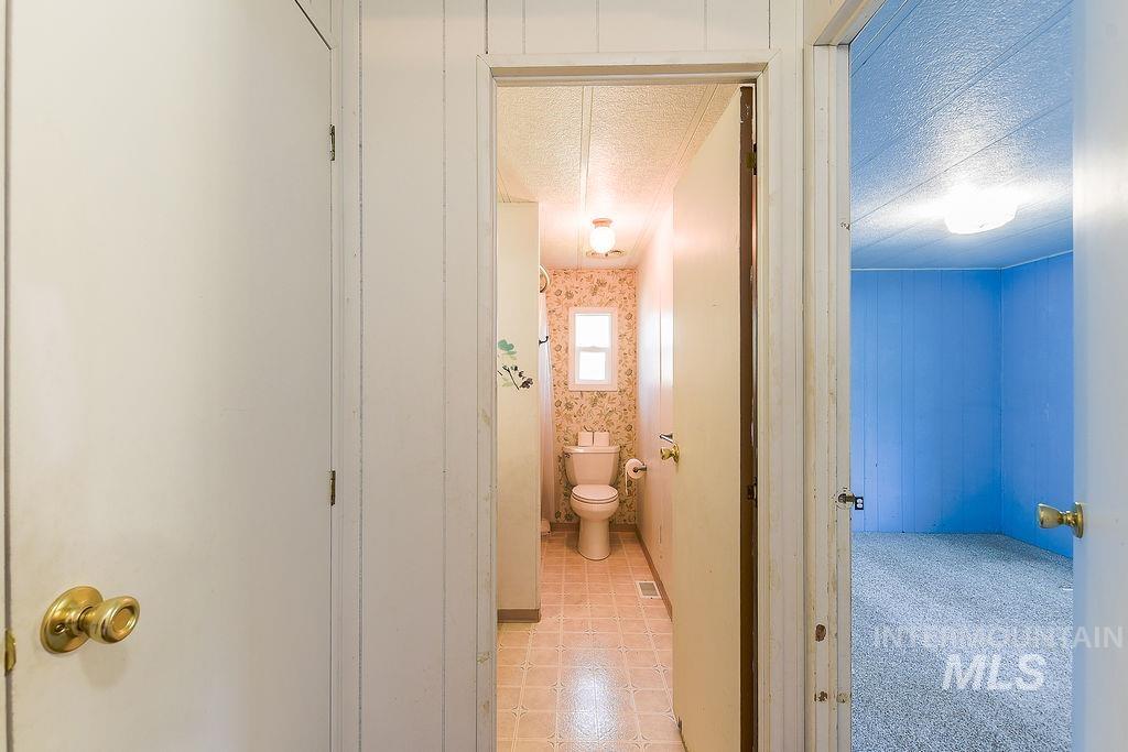 Hallway featuring a textured ceiling, light colored carpet, and wallpapered walls