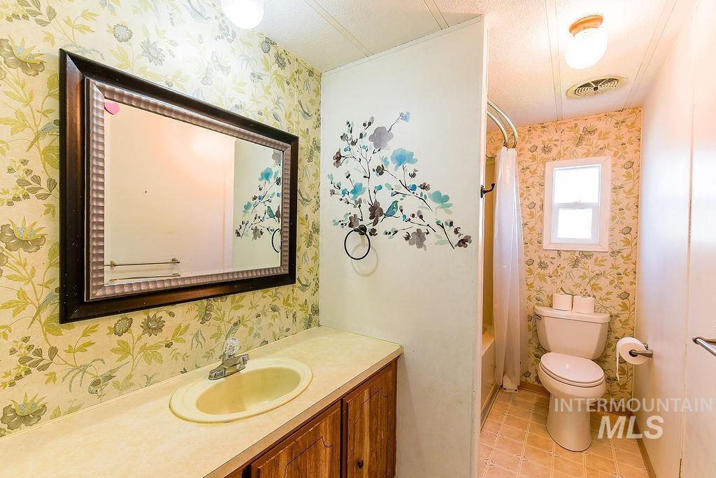 Bathroom with wallpapered walls, vanity, shower / tub combo, and light tile patterned flooring
