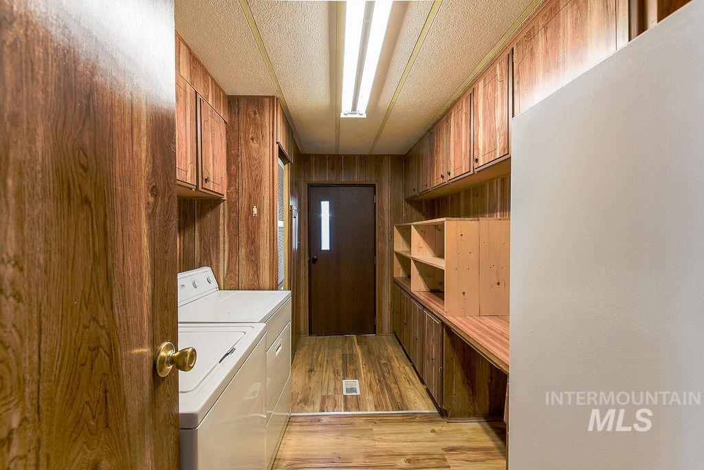 Laundry area featuring light wood-style flooring, wood walls, washing machine and dryer, and cabinet space