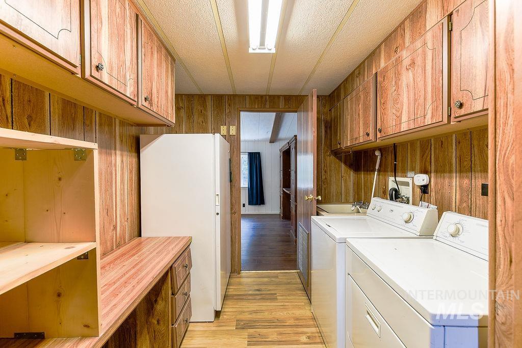 Laundry area featuring light wood-type flooring, wood walls, separate washer and dryer, a textured ceiling, and cabinet space