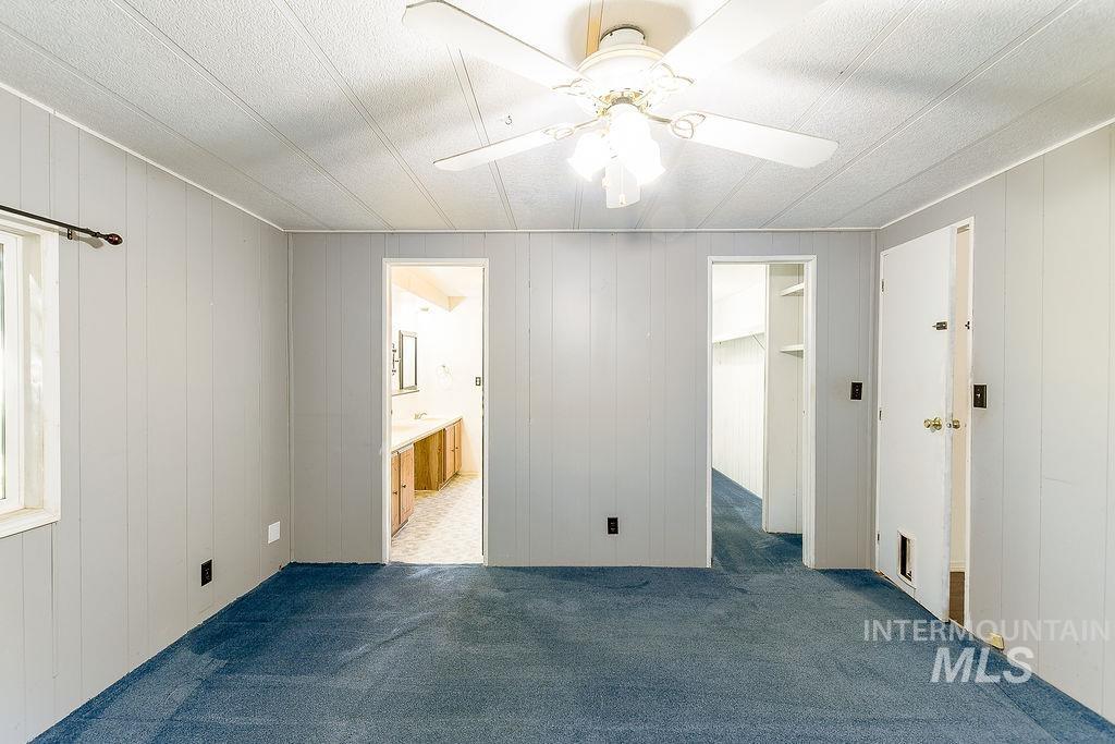 Unfurnished bedroom featuring carpet floors, wood walls, a walk in closet, a ceiling fan, and connected bathroom