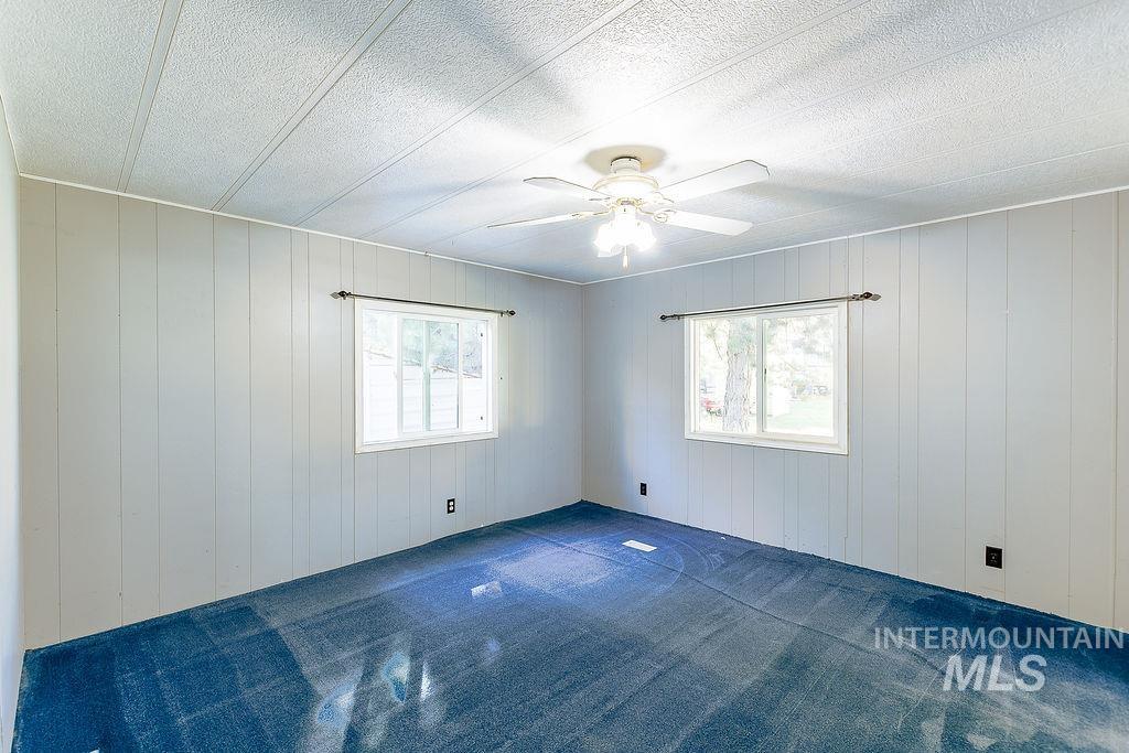 Unfurnished room with healthy amount of natural light, carpet, ceiling fan, and wooden walls